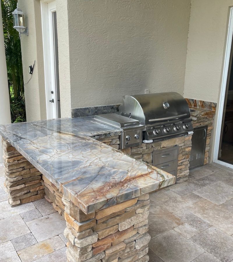 High-end outdoor kitchen remodel with natural stone finish, built-in stainless steel grill, and custom hardscaping in Palm Beach Gardens by The Beatles Kitchen & Bath.