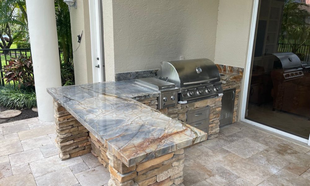84A0A3D4-C821-40BA-974A-39FB30AB14B3 High-end outdoor kitchen remodel with natural stone finish, built-in stainless steel grill, and custom hardscaping in Palm Beach Gardens by The Beatles Kitchen & Bath.